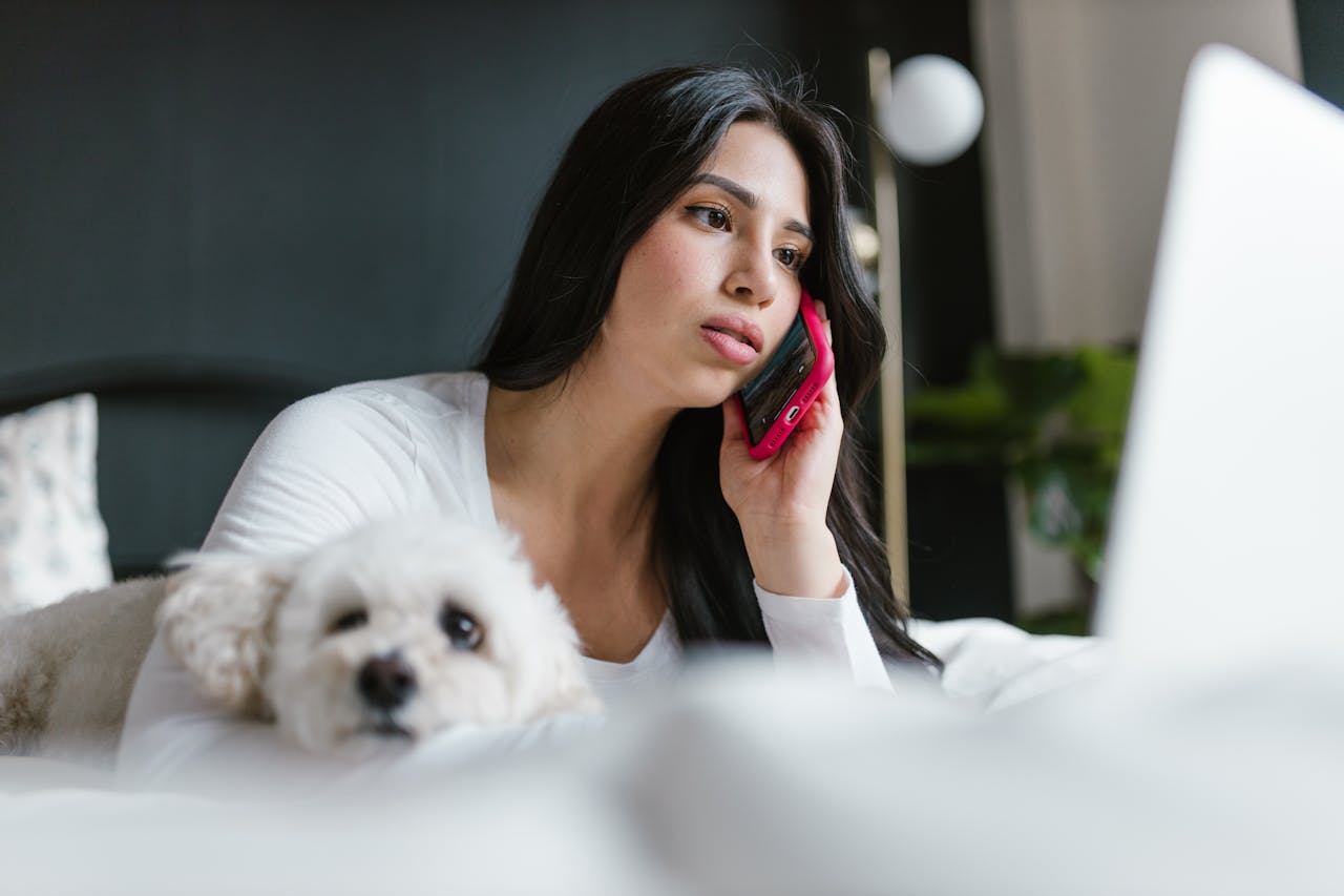 Nő fekszik az ágyon a kutyájával és telefon teszi fel néhány kérdését a szakembernek.