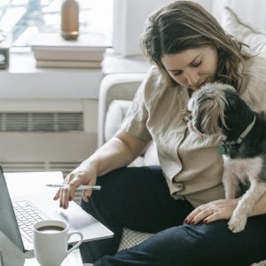Egy nő otthon eredménygaranciás szolgáltatást keres a laptopján a kutyájával, meghitt munkakörnyezetet teremtve.